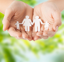 Wall Mural - people and relations concept - close up of female hands with paper family pictogram over green natural background