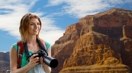 Wall Mural - travel, tourism and photography concept - happy young woman with backpack and camera photographing over grand canyon national park background