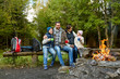 © Syda Productions - family, camping and tourism concept - happy mother, father, son and daughter sitting on bench and drinking hot tea from cups at camp fire in woods