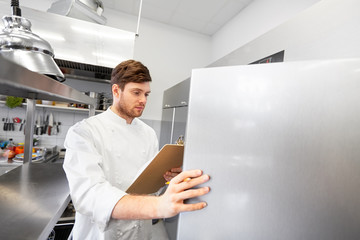 cooking, profession and people concept - male chef cook with clipboard doing inventory and looking to fridge at restaurant kitchen