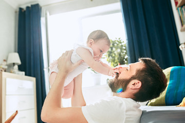 Wall Mural - Proud father holding his newborn baby daughter up in the air at home