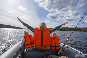 girl in a life jacket floating on the boat with his hands up. children in life jackets sitting next