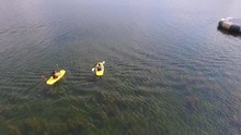 Aerial Shot Of Two Boys Paddling Kayaks On A Clear Blue Lake In The Summer