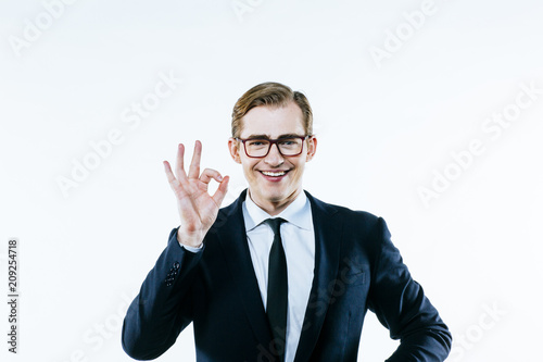 Fotografie, Obraz Portrait of a young man in suit and tie making a 'perfect' hand gesture, on whit