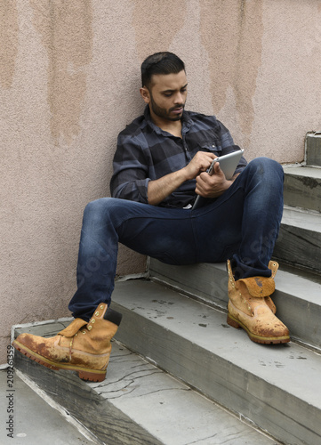 Fotografie, Obraz young man sitting on stairs with a tablet computer