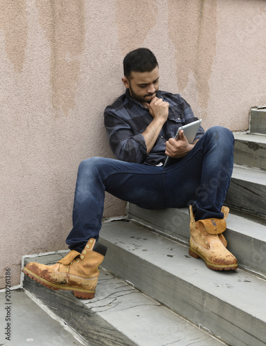 Fotografie, Obraz young man sitting on stairs with a tablet computer