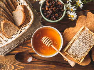 Wall Mural - Honey pot and dipper at rustic table with bread, raisins, chamomile and Honey comb, top view