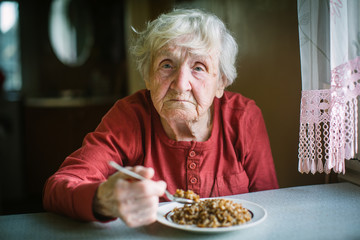 Wall Mural - Elderly woman eats buckwheat porridge sitting at the table.