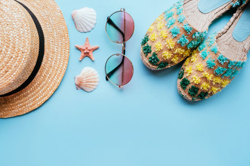 Wall Mural - Summer fashion flatlay with gradient round sunglasses, straw hat and espadrille sandals on the blue background with starfish and shells. Perfect beach set for holidays on the sea. Marina style.