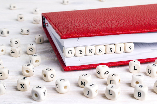 Word Genesis written in wooden blocks in red notebook on white wooden table.