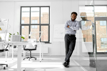 Wall Mural - business and people concept - smiling african american businessman at office glass wall