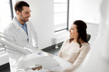 Wall Mural - medicine, dentistry and healthcare concept - male dentist talking to female patient and discussing teeth treatment at dental clinic office