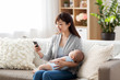 © Syda Productions - family, technology and motherhood concept - happy smiling young asian mother with sleeping baby and smartphone at home