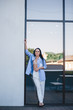 © Денис Кипкаев - A beautiful woman in a shirt and pants is standing by the mirror window of the balcony of the building.