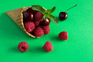 Wall Mural - Ice cream cone  with raspberries and cherry on the green  background