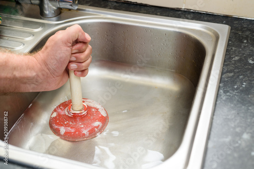 Fotografía Man holding a plunger with one hand and water in sink, used to clean a clogged /