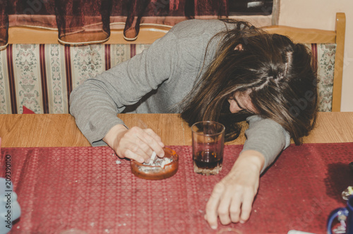 Fotografia Drunk housewife drinking alcohol drink and smoking cigarette in her home on the