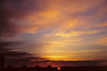 Wall Mural - Beautiful cloudy dramatic morning sky above silhouette of city buildings. Picturesque dawn in city. Background of varicolored clouds. Unimaginable fantasy sunrise in heaven.