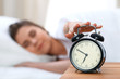 © rogerphoto - Sleepy young woman stretching hand to ringing alarm willing turn it off. Early wake up, not getting enough sleep concept