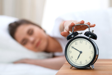 Sleepy young woman stretching hand to ringing alarm willing turn it off. Early wake up, not getting enough sleep concept