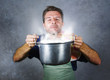 © TheVisualsYouNeed - young attractive happy and proud home cook man cooking soup holding kitchen pot smelling the meal aroma gesturing delighted and satisfied