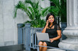 © Danon - Portrait of a young, attractive and photogenic Indian Asian business woman talking on her phone with her laptop computer on her lap. She is seated in a bench during the day as she takes her call.