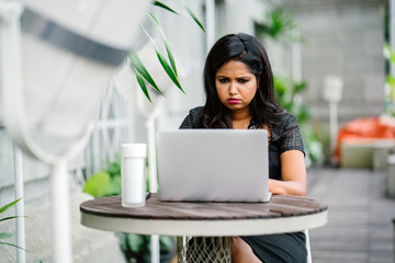 A confident and successful Indian woman (professional or business woman) is sitting and working on her laptop in the day. 