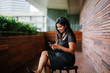 © Danon - A confident and attractive Indian Asian woman is typing and using her smartphone as she sits on a chair outdoors during the day.