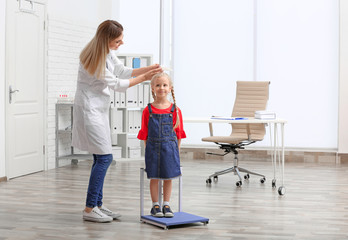 Wall Mural - Doctor measuring little girl's height in hospital