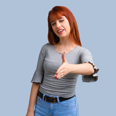 Young redhead girl handshaking after good deal on blue background