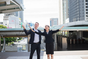 Asian businessman and businesswoman stand and raising up two hands to cheerful and celebrated for successful in career and mission. concept of winner and competition.