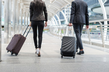 Wall Mural - back of businessman and businesswoman walk together with luggage on the public street, business travel concept