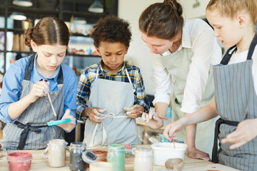 Wall Mural - Several schoolkids and teacher in aprons choosing paints to paint up clay mugs they made by themselves