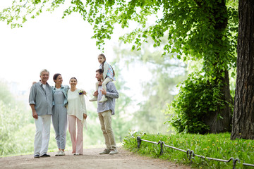 Family of five spending summer day in park by walking under green foliage