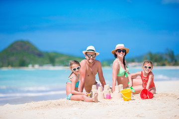 Family of four making sand castle at tropical white beach