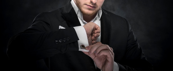 Elegant young fashion man looking at his cufflinks.