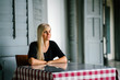 © Danon - A very attractive blonde lady sitting at a table inside an old,colonial building . She patiently waiting for someone while enjoying the moment.