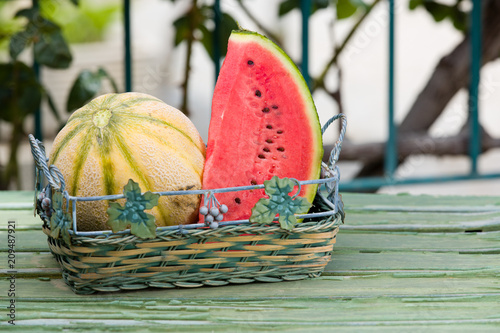 Fotografiet Seasonal fresh fruits, watermelon and rockmelon in basket on garden table