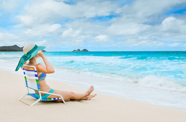 Summer beach vacation. Young female sitting on chair relaxing on the beach. 