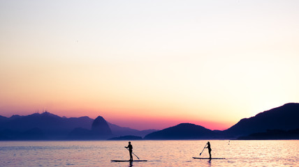 Two people practice stand-up paddle at dusk surrounded by paradisiacal coasts in Niteroi, RJ (Brazil)