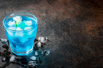 Colorful summer beverage, iced blue lagoon alcohol cocktail drink with lime and mint, bark background copy space