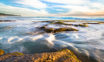 Wall Mural - Long exposure of ocean waves flowing over rocky tidepools at sunset on Johanna Beach in the Great Otway National Park, Victoria, Australia.