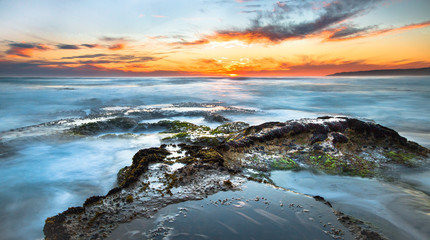 Wall Mural - Long exposure of ocean waves flowing over rocky tidepools at sunset on Johanna Beach in the Great Otway National Park, Victoria, Australia.