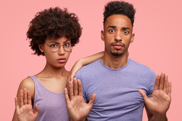 Poster - Horizontal shot of serious African American wife and husband show stop gesture, deny something with nagative facial expression, stand against pink background. Companionship and body language