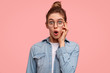© WHstudio Leushin N - Portrait of amazed cute female stares at camera, keeps mouth wide opened, can`t believe in her failure, stands against pink background, dressed in denim jacket. People, reaction and emotions concept