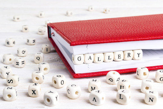 Word Gallery written in wooden blocks in red notebook on white wooden table.