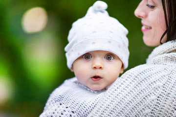 Closeup portrait of mom hugging amazed baby outdoors at green background.