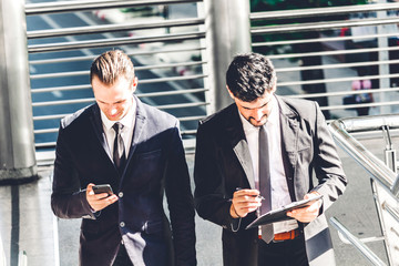 Two smiling businessman coworkers in black suit talking and walking.business people discussing strategy in the modern city