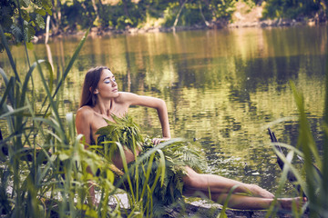 Summer heat. Beautiful young girl in a forest lake, open clothes from fern leaves, perfectly combined with nature. A person in the form of a fantasy elf, dryads, cosplay of a character.