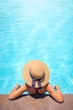 Woman with brown hat relaxing in swimming pool with blue water during a sunny day , holiday concept